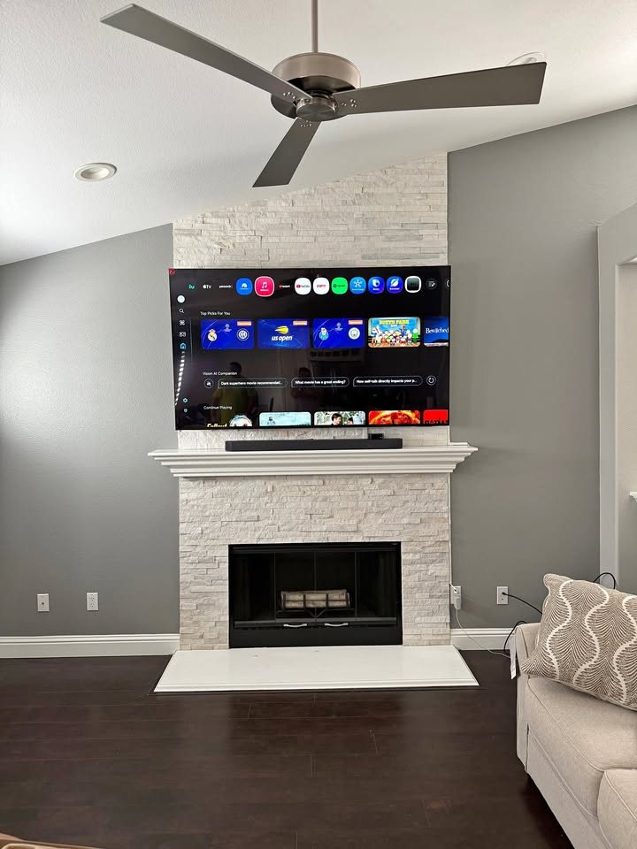 TV and soundbar mounted above a white stone fireplace under a vaulted ceiling